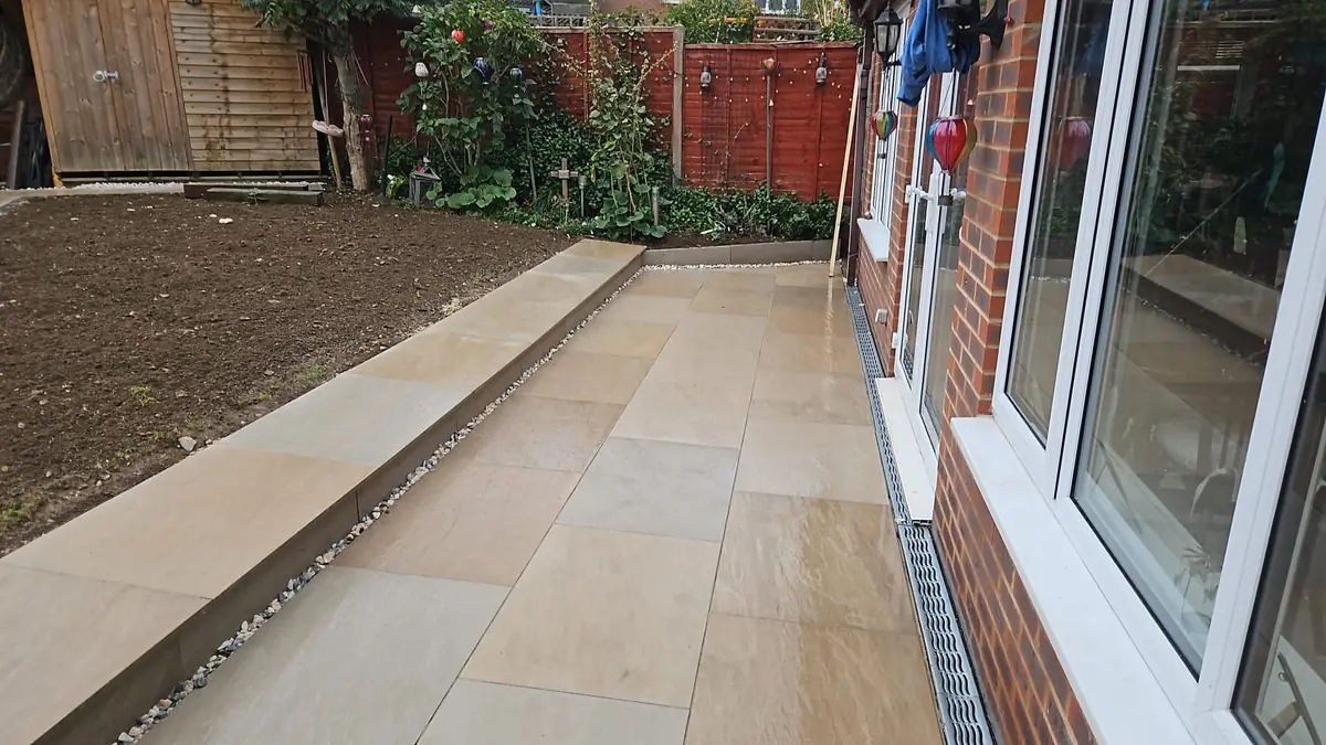 Buff paving patio along the back of a house, with a linear drainage channel beneath the patio doors