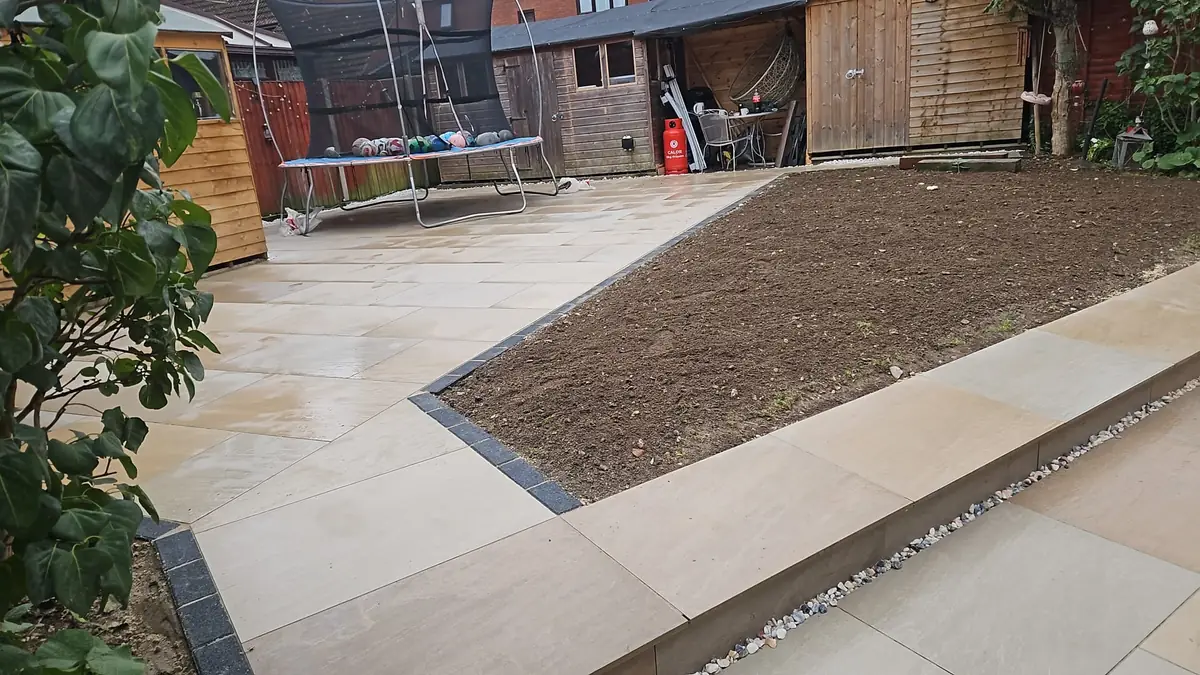 Buff paving patio edged with dark grey kerbs where it meets the garden bed, with a raised level in the foreground