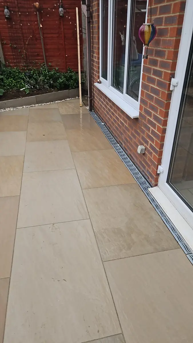 Linear drainage channel set into a buff paving patio beneath the patio doors