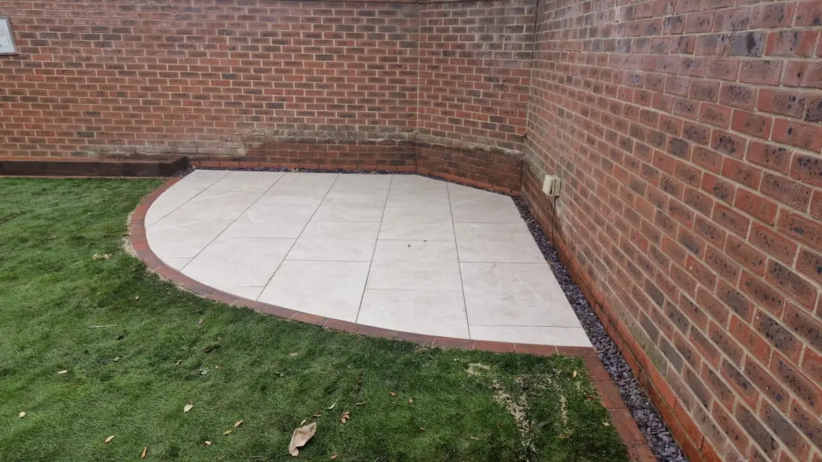 Curved porcelain sitting area in the corner of the garden, edged in brick against the boundary wall