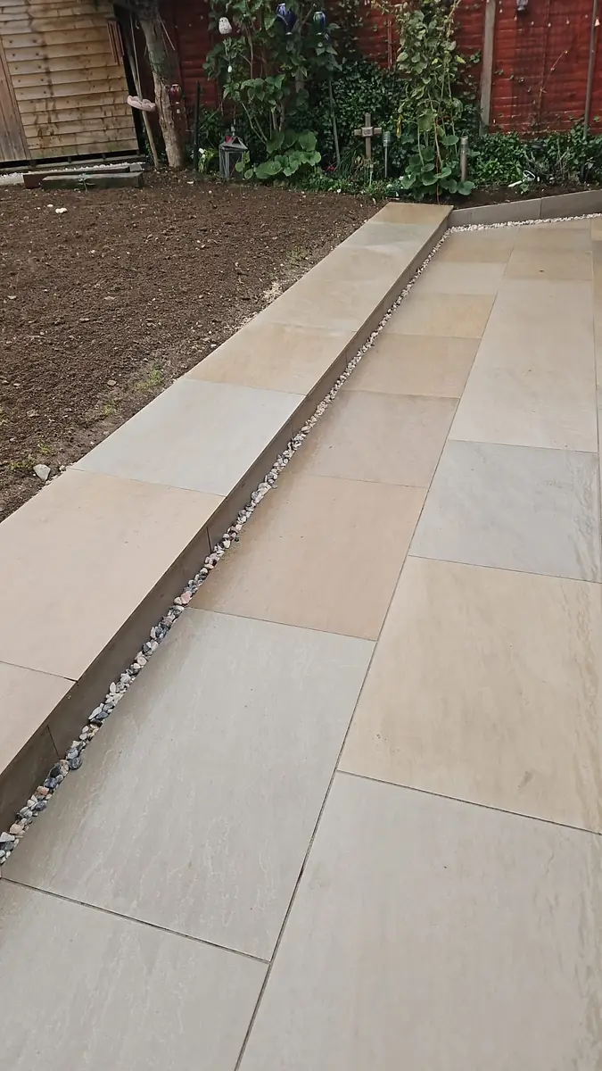 Two-level patio in buff paving slabs, with a step down to the lower level and a gravel strip along its edge